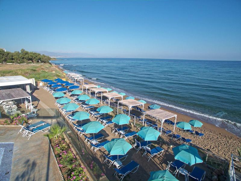 Beach with blue umbrellas and lounge chairs by calm sea under clear sky.