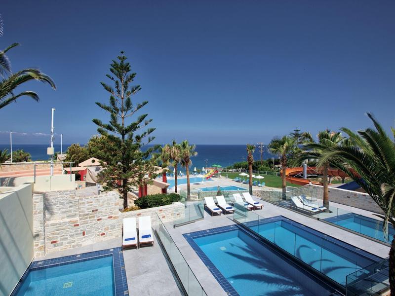 Modern outdoor pool area with lounge chairs and a view of the sea under a clear sky.