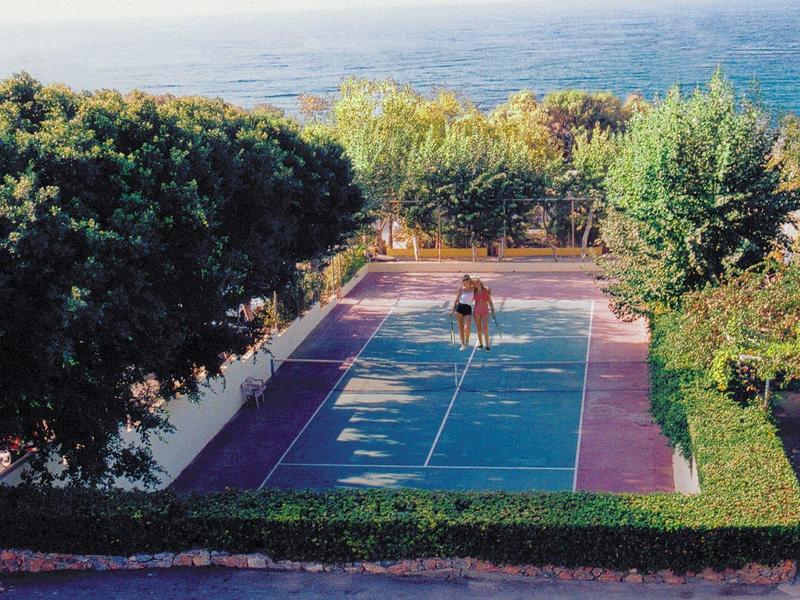 A tennis court surrounded by trees with a view of the sea in the background.