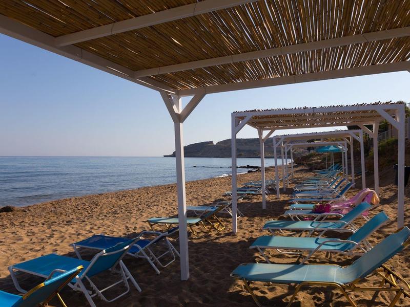 Beach with blue sun loungers and shade structures on sandy shore, calm sea in the background.