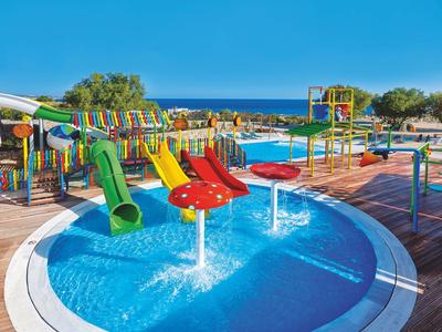 Piscina per bambini con scivoli d'acqua e giochi colorati sotto un cielo limpido vicino al mare.