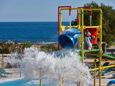 Bambini che giocano su un colorato parco giochi acquatico con scivolo vicino alla piscina accanto al mare.