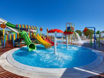 Area giochi acquatica colorata con scivoli e fontane sotto un cielo azzurro limpido.