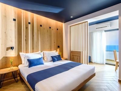 Camera d'hotel moderna con letto matrimoniale, pareti in legno e zona salotto con luce calda.