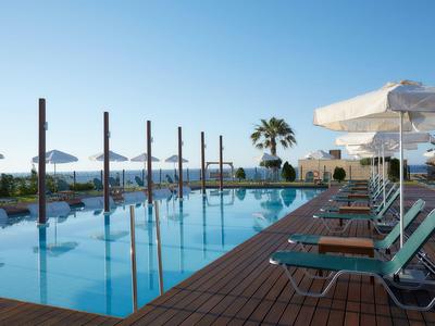 Piscina esterna moderna con sdraio e ombrelloni accanto al mare calmo e alle palme.
