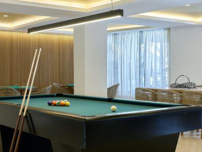 Tavolo da biliardo moderno in una stanza luminosa con grandi finestre e illuminazione a soffitto.