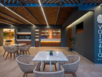 Area lounge moderna dell'hotel con tavoli, sedie e bancone illuminato sotto soffitto in legno.
