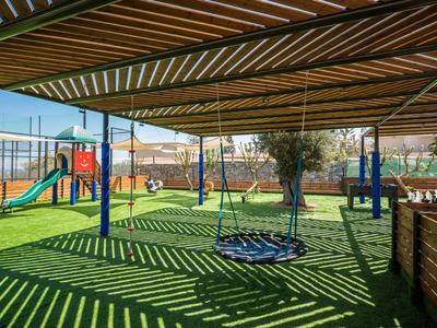 Area giochi ombreggiata con scivolo e altalena in una giornata di sole.