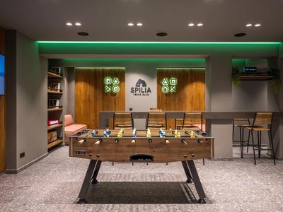 Sala giochi moderna con calcio balilla, zona salotto e bar con sgabelli.