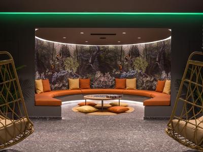 Lounge accogliente con divano arancione curvo, sedie in rattan e illuminazione verde soffusa.