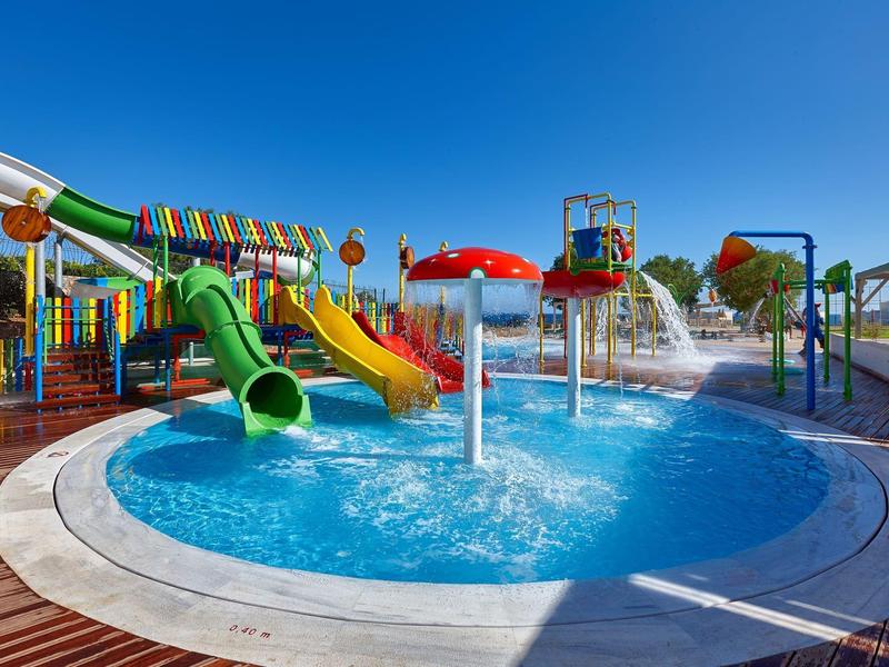 Area giochi acquatica colorata con scivoli e fontane sotto un cielo azzurro.