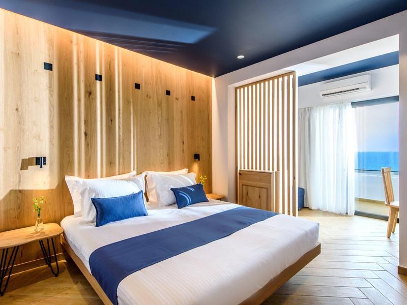 Camera d'hotel moderna con letto matrimoniale, pareti in legno e zona salotto con luce calda.