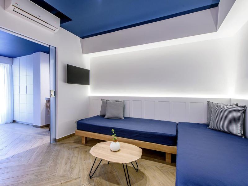 Camera d'hotel moderna con divani blu, TV a schermo piatto e arredamento minimalista.