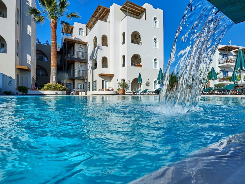 Piscina dell'hotel moderna con cascata e edifici bianchi con tempo soleggiato.