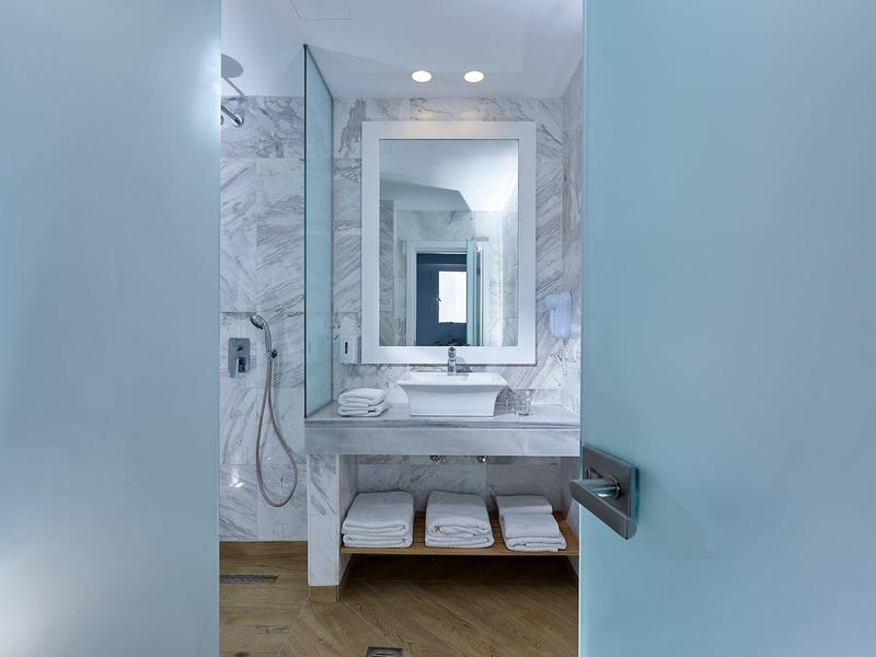 Bagno moderno con grande specchio, lavabo in marmo e asciugamani su mensola in legno
