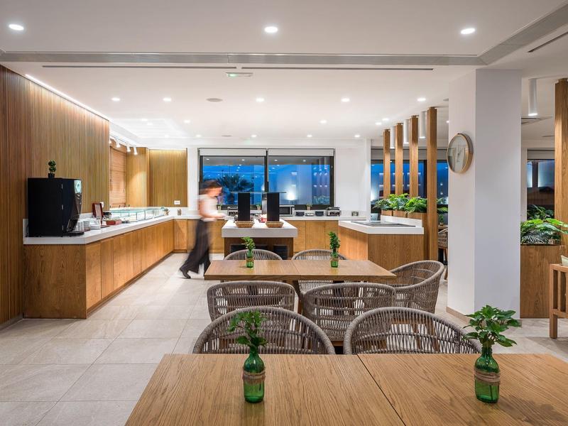 Ristorante d'hotel moderno e luminoso con mobili in legno e piante verdi.