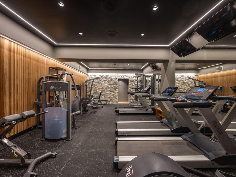 Palestra moderna con tapis roulant, attrezzi per la forza, pareti in legno e specchi.