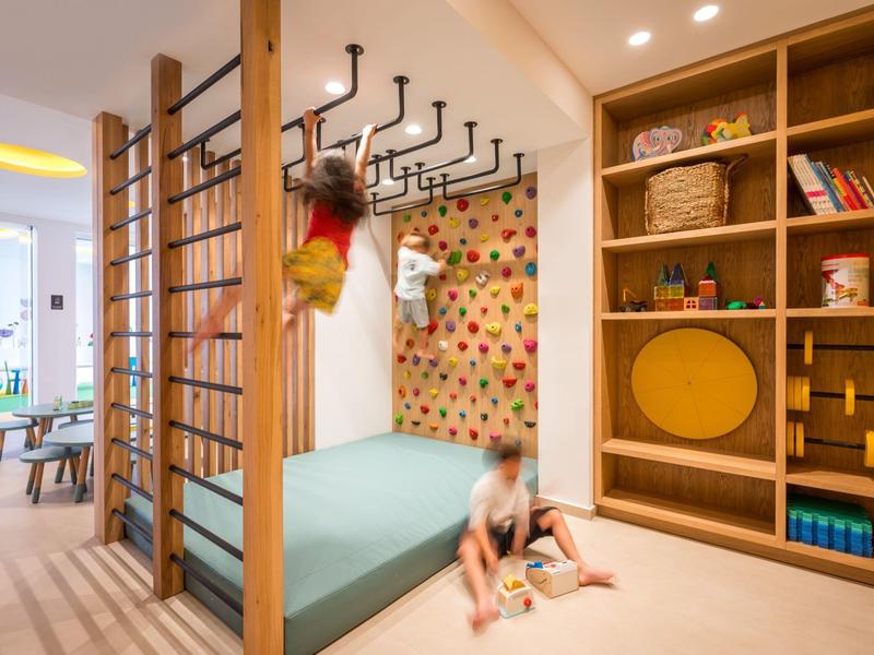 Bambini che giocano in un'area di arrampicata e gioco moderna e luminosa con prese colorate e scaffali.