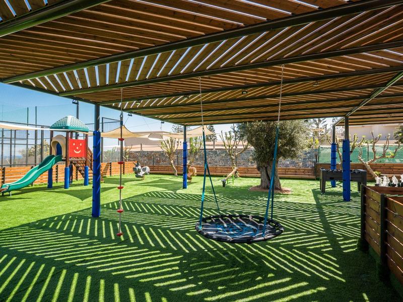 Area giochi ombreggiata con scivolo e altalena in una giornata di sole.