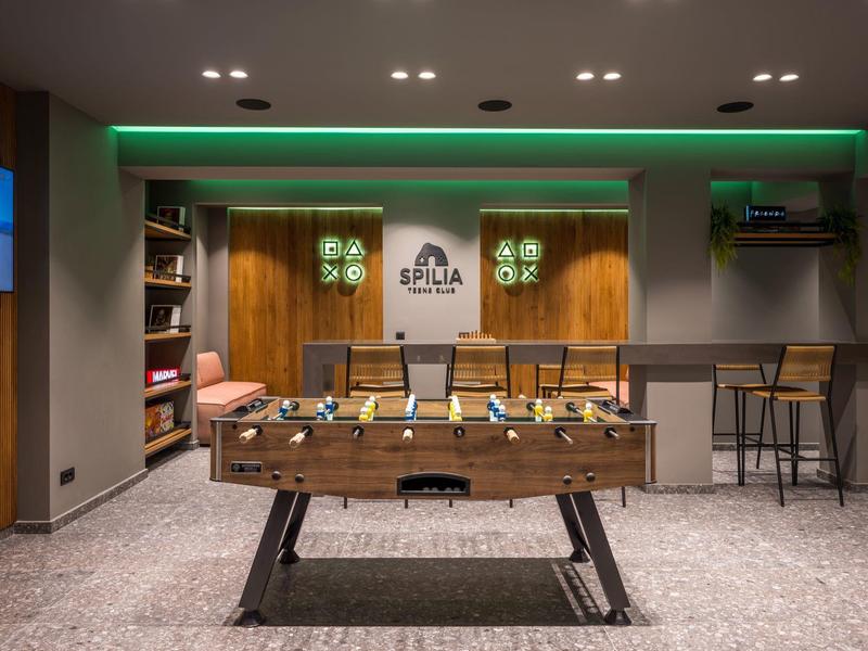 Sala giochi moderna con calcio balilla, zona salotto e bar con sgabelli.