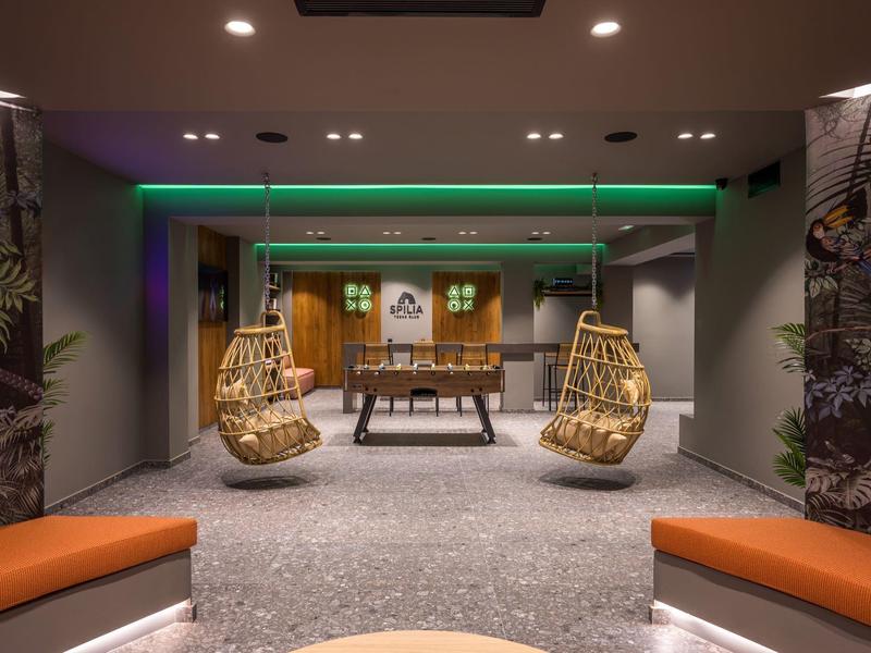 Lounge dell'hotel moderna con sedie sospese, calcio balilla e illuminazione soffusa in un'atmosfera accogliente.