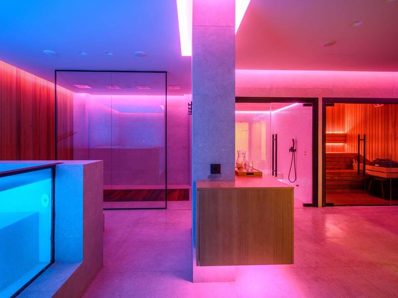 Area benessere moderna con sauna e piscina illuminata a colori.
