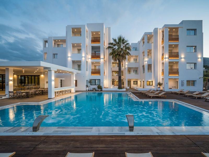 Complesso alberghiero moderno con piscina illuminata e lettini al crepuscolo.