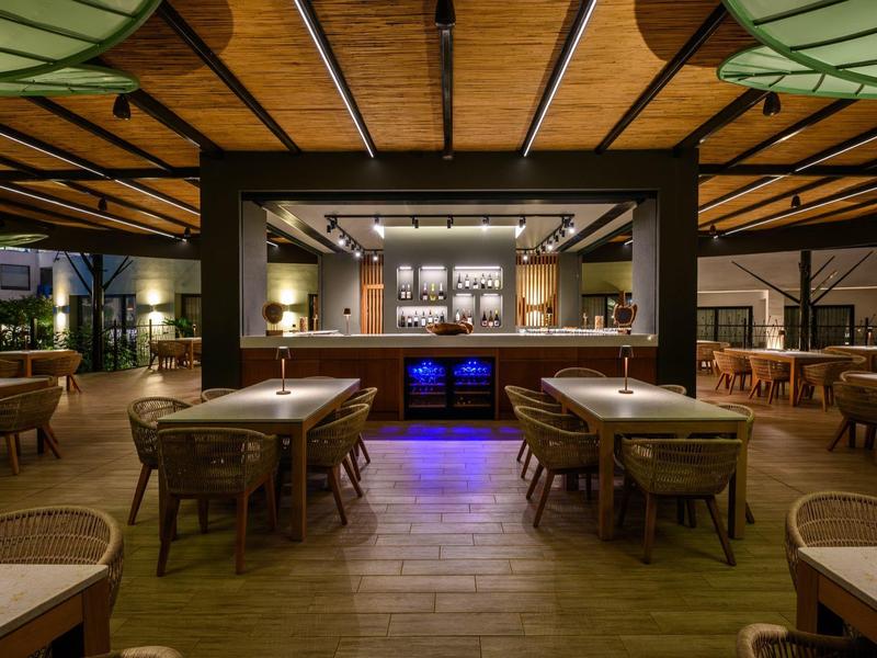 Ristorante moderno con tavoli e sedie in legno e bancone ben illuminato al centro.