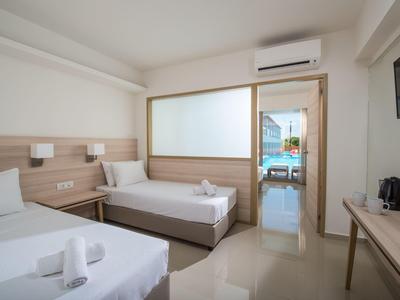 Camera d'hotel luminosa con due letti singoli, aria condizionata, TV e terrazza con vista mare.