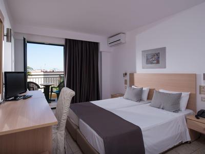 Camera d'hotel luminosa con letto matrimoniale, scrivania, sedia e balcone con vista sulla città.