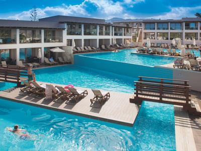 Nowoczesny basen hotelowy z leżakami, gośćmi i czystą niebieską wodą pod błękitnym niebem.