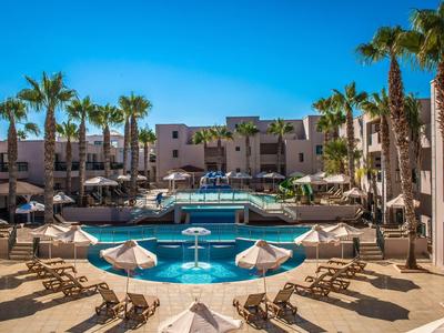 Piscina moderna dell'hotel con lettini e palme sotto un cielo azzurro limpido.