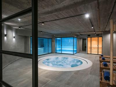 Area benessere moderna con jacuzzi rotonda, grandi finestre e sedie in legno