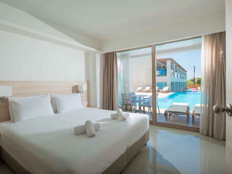 Camera d'hotel luminosa con letto matrimoniale che si affaccia su piscina e terrazza.