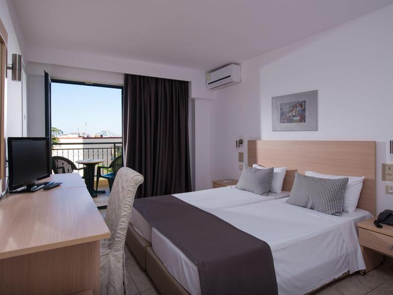 Camera d'hotel luminosa con letto matrimoniale, scrivania, sedia e balcone con vista sulla città.