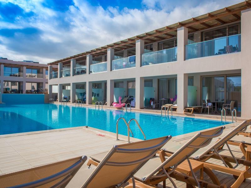 Hotel moderno con grande piscina all'aperto e lettini sotto un cielo azzurro.