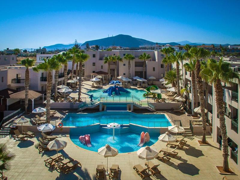 Vista di una piscina dell'hotel con lettini, palme e montagne sullo sfondo.