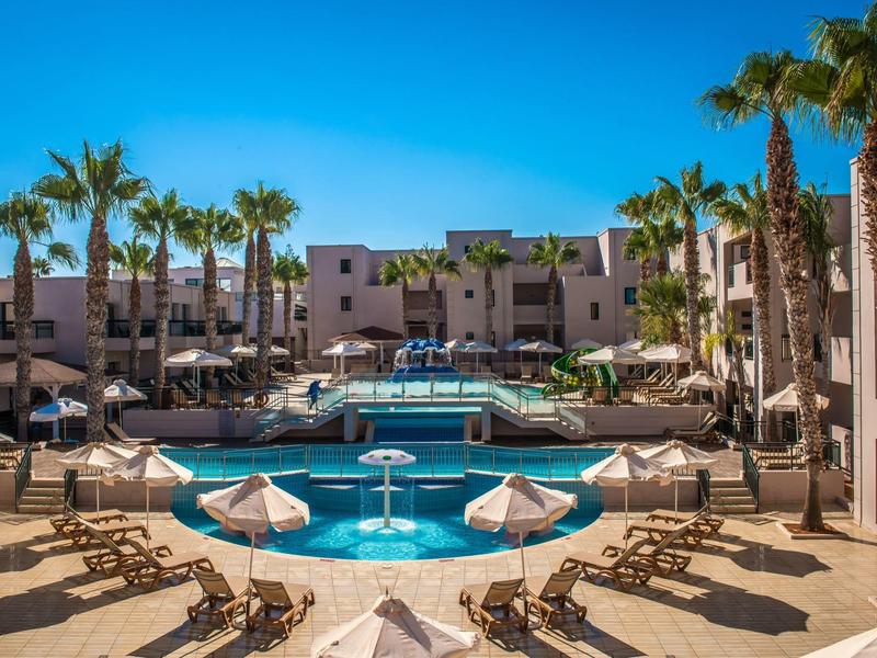 Piscina moderna dell'hotel con lettini e palme sotto un cielo azzurro limpido.