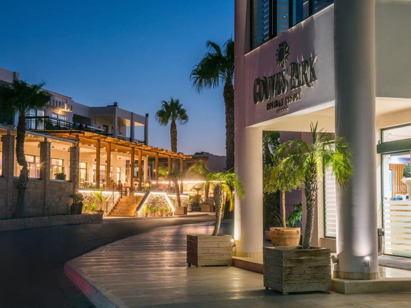 Ingresso dell'hotel illuminato con palme e design moderno al crepuscolo.