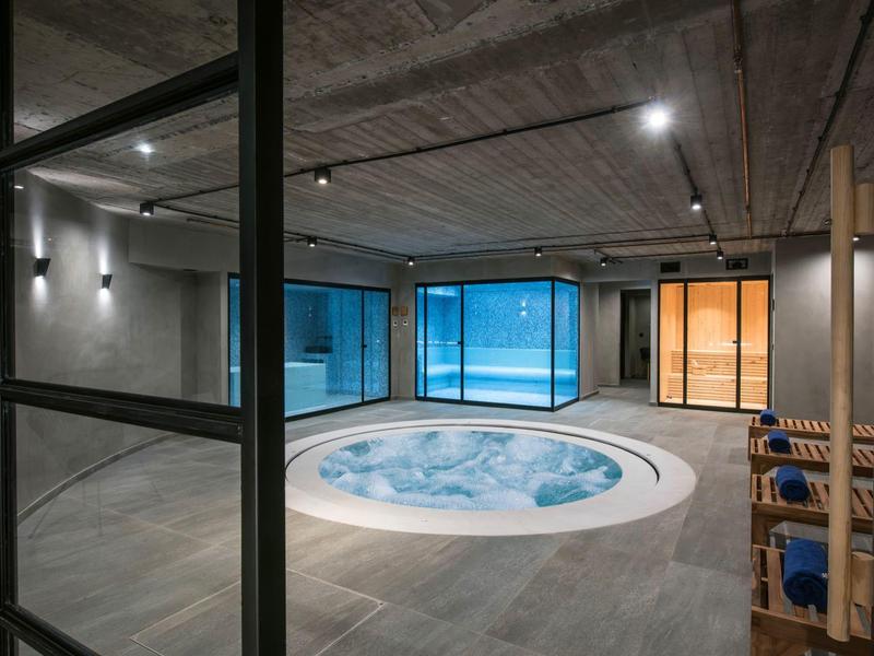 Area benessere moderna con jacuzzi rotonda, grandi finestre e sedie in legno