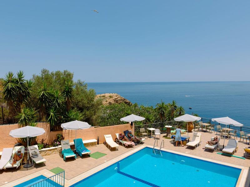 Espace piscine avec transats et parasols surplombant la mer sous un ciel dégagé.