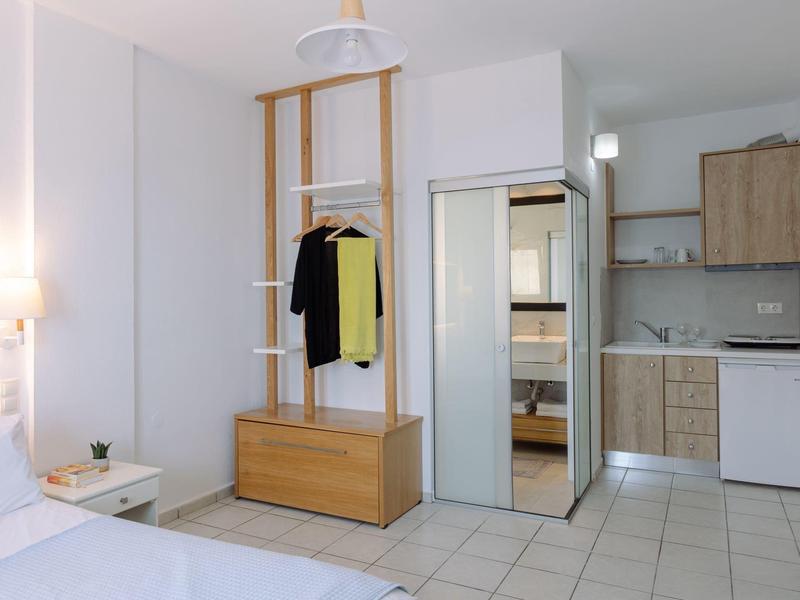Chambre d'hôtel compacte avec armoire, lit, petite kitchenette et mobilier moderne.