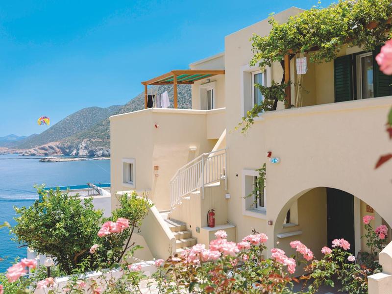 Bâtiment blanc avec balcon et fleurs en fleurs avec vue sur la mer et les montagnes.