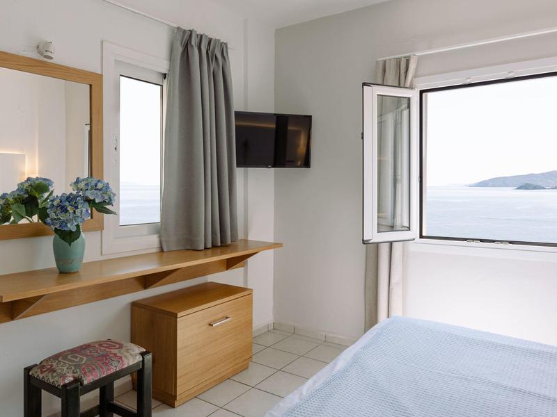 Chambre d'hôtel lumineuse avec bureau, télévision et fenêtre ouverte sur la mer.