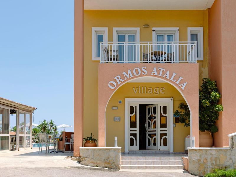 Entrée d'un hôtel orange avec balcon et enseigne 'Ormos Atalia Villas'