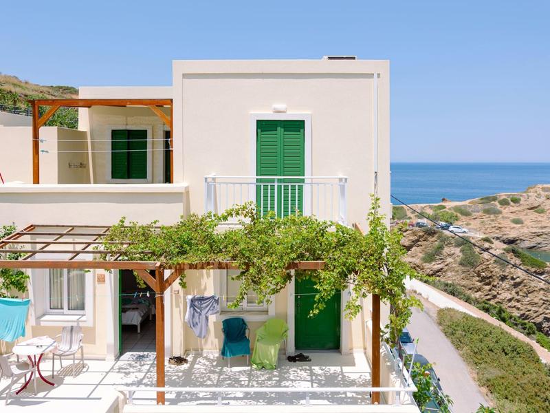 Bâtiment d'hôtel blanc avec portes vertes et pergola avec plantes grimpantes au bord de la mer.