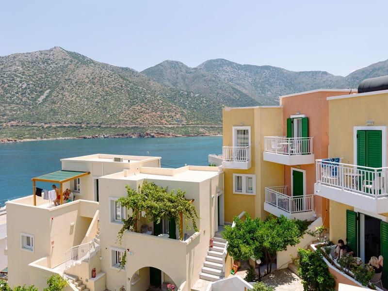 Bâtiments jaunes et blancs sur la côte avec vue sur la mer et montagnes en arrière-plan.