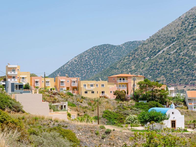 Village avec petites maisons et chapelle devant des montagnes boisées sous un ciel clair.