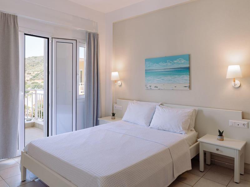 Chambre d'hôtel lumineuse avec lit double, tables de chevet et vue sur la mer depuis la fenêtre.