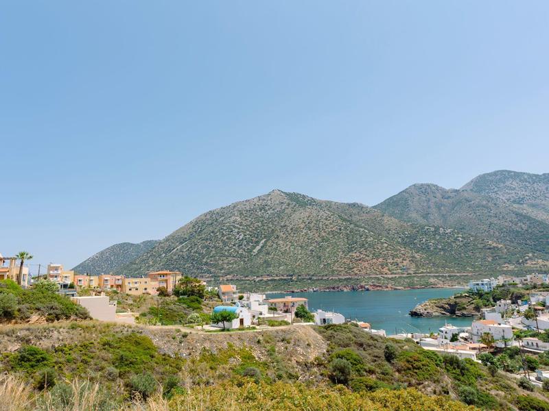 Paysage avec montagnes, mer et maisons le long du rivage sous un ciel clair.